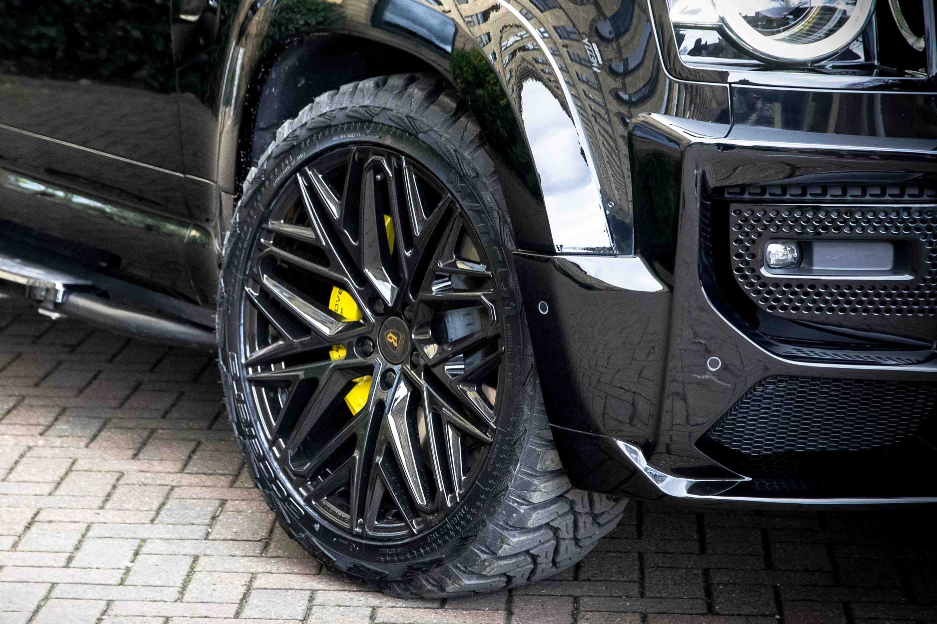 Front quarter detail view of a Black Land Rover Defender 90 L663. Parked outside a restaurant Fitted with Barugzai Shuracan 22” alloy wheels, in Gloss Black.