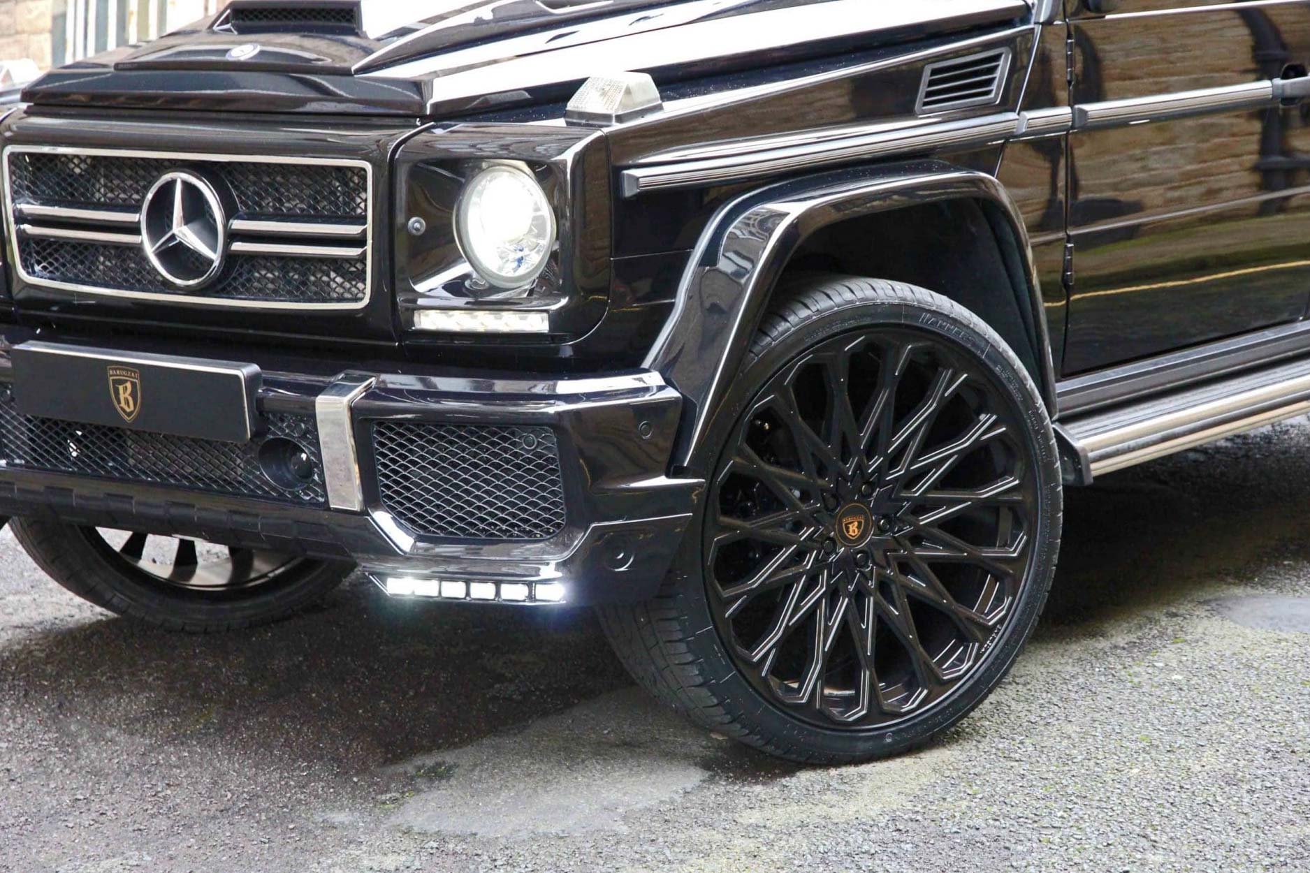 Front quarter detail view of a Black Mercedes G Wagon W463 Gen I 1990-2017. Shot outside a city street. Fitted with Barugzai Majestic 24” alloy wheels, in Gloss Black.