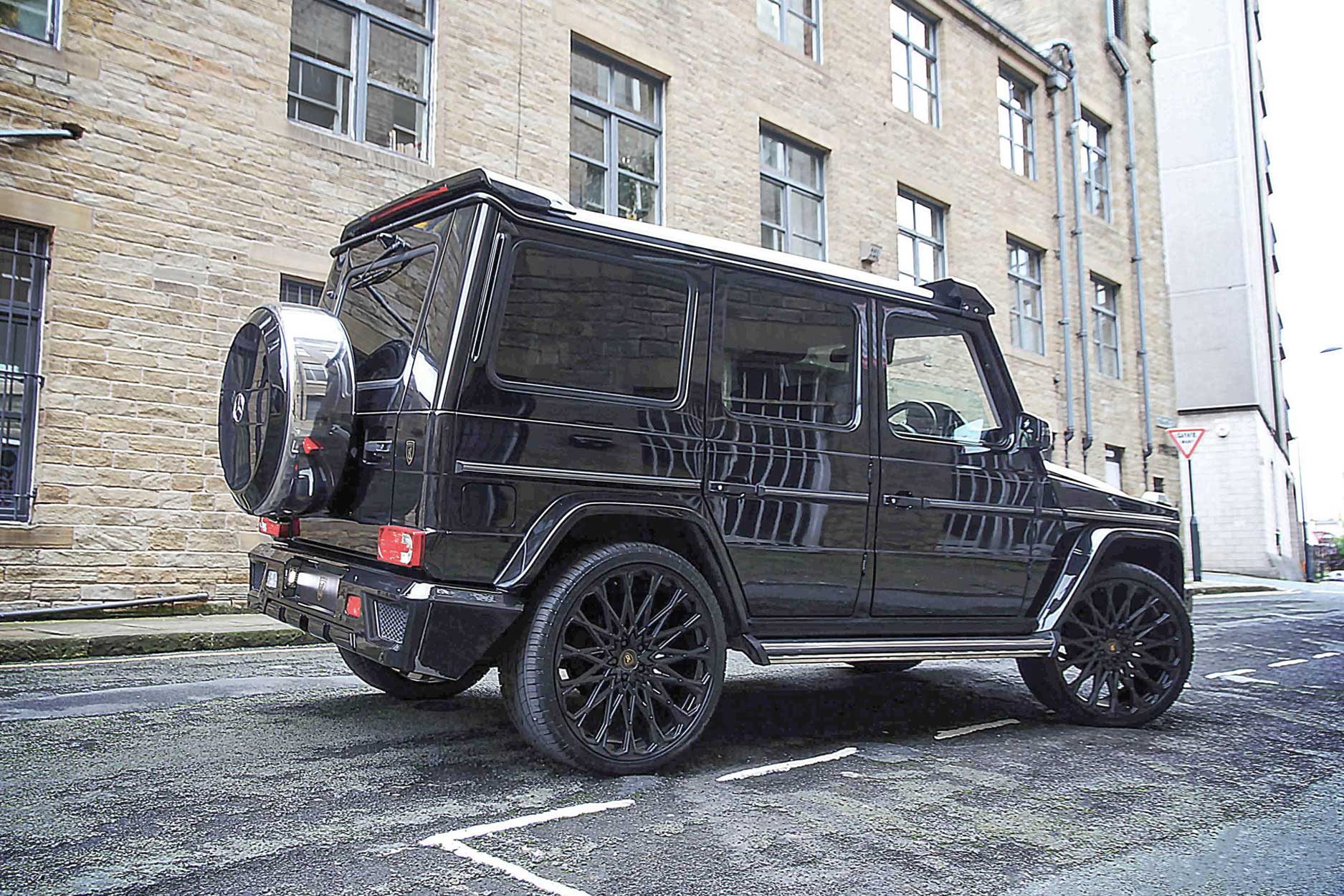 Rear quarter detail view of a Black Mercedes G Wagon W463 Gen I 1990-2017. Shot outside a city street. Fitted with Barugzai Majestic 24” alloy wheels, in Gloss Black.
