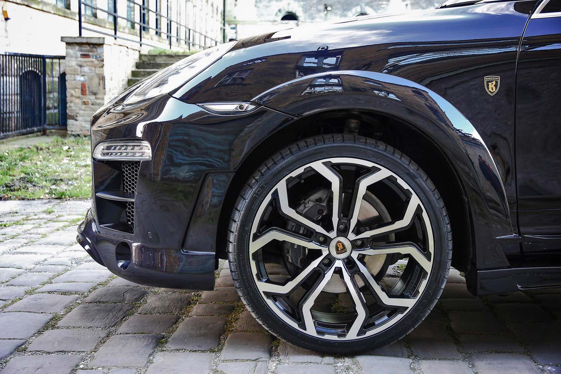 Side detail view of a Blue Porsche Cayenne 92A 2011-2018. Shot outside an old mill. Fitted with Barugzai Opium 22” alloy wheels, in Gloss Black Polished Face.