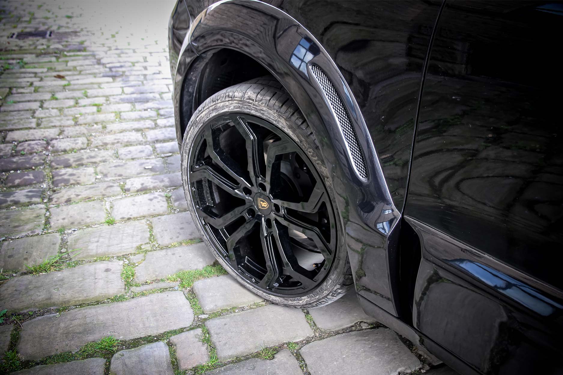 Side quarter detail view of a Blue Porsche Cayenne 9YA 2019+ . Shot outside an old mill. Fitted with Barugzai Opium 22” alloy wheels, in Gloss Black