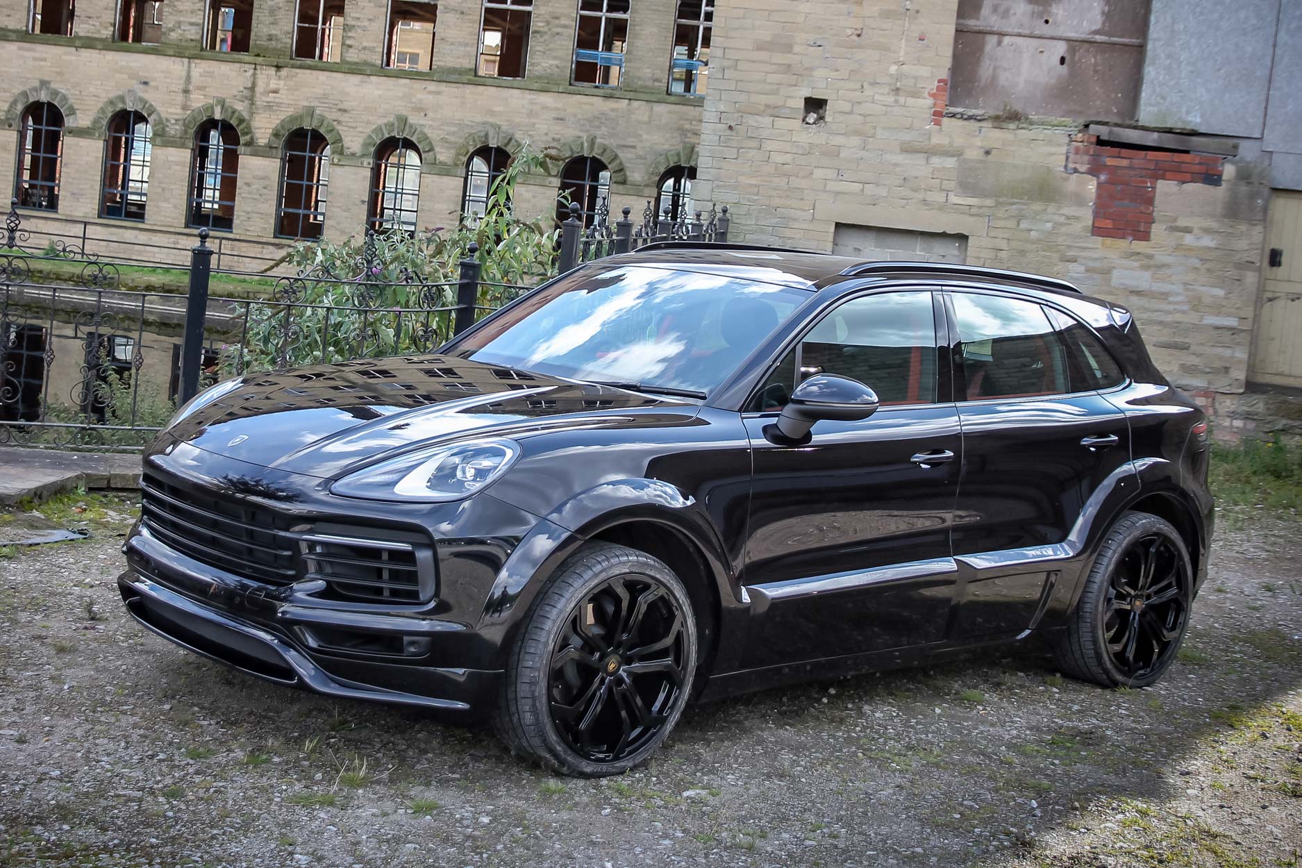 Front quarter view of a Blue Porsche Cayenne 9YA 2019+ . Shot outside an old mill. Fitted with Barugzai Opium 22” alloy wheels, in Gloss Black