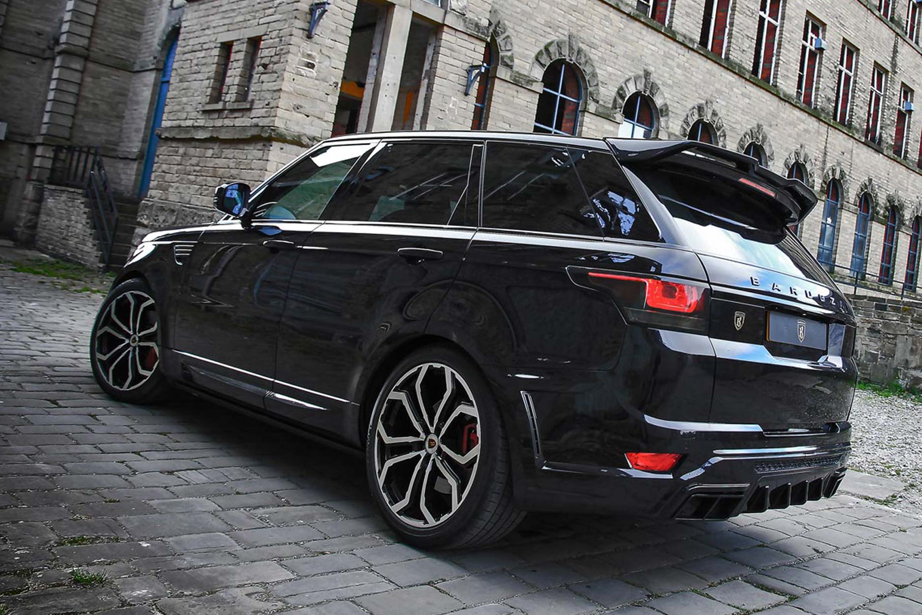 Rear quarter view of a Black Range Rover Sport L494 2013-2017. Shot outside an old mill. Fitted with Barugzai Opium 22” alloy wheels, in Gloss Black Polished Face.
