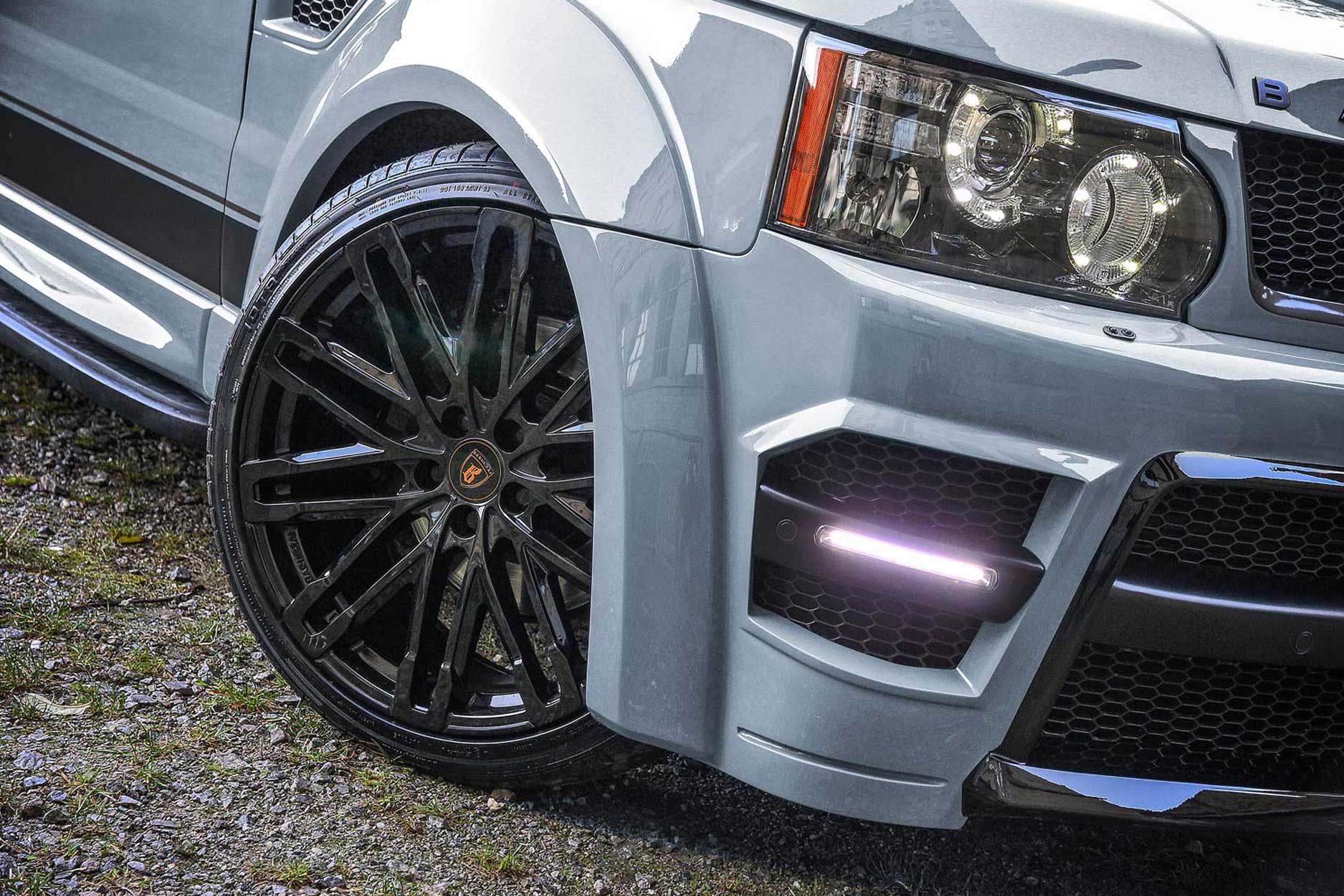 : Front quarter detail view of a Nardo Grey Range Rover Sport L320 2009-2012. Shot outside an old mill. Fitted with Barugzai Dawn 22” alloy wheels, in Gloss Black.