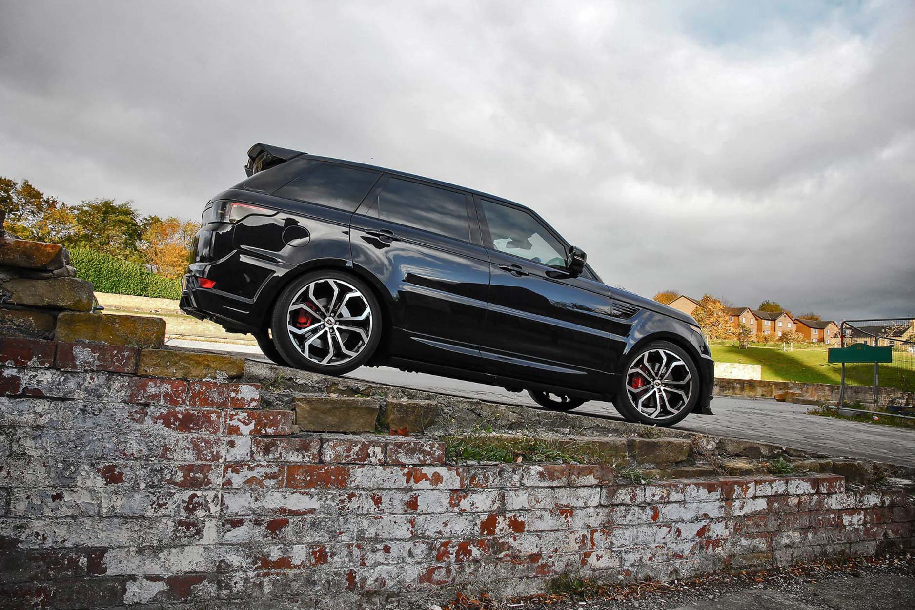 Side quarter view of a Black Range Rover Sport L494 2013-2017. Shot outside an old mill. Fitted with Barugzai Opium 22” alloy wheels, in Gloss Black Polished Face.