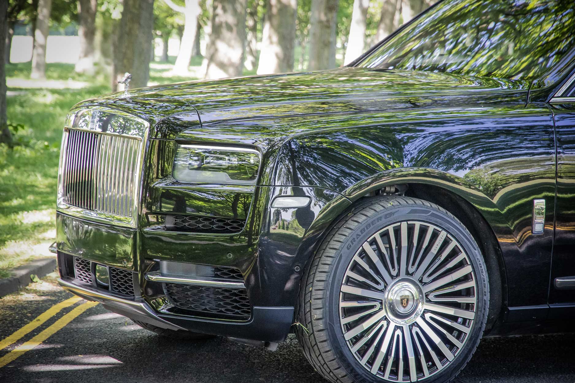 Front quarter detail view of a Black Rolls Royce Cullinan 2018+. Shot outside a large lawn backdrop. Fitted with Barugzai Casanova 22/23” alloy wheels, in Gloss Black Polished Face.