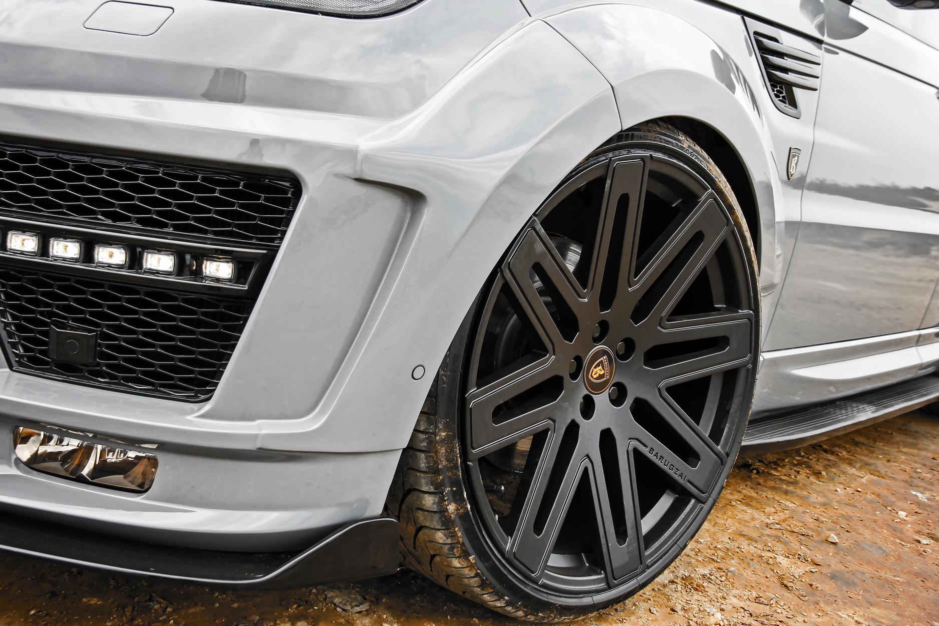 Front quarter detail view of a Nardo Grey Range Rover Sport L494 2013-2017. Shot outside a quarry. Fitted with Barugzai EXEL 24” alloy wheels, in Gloss Black.