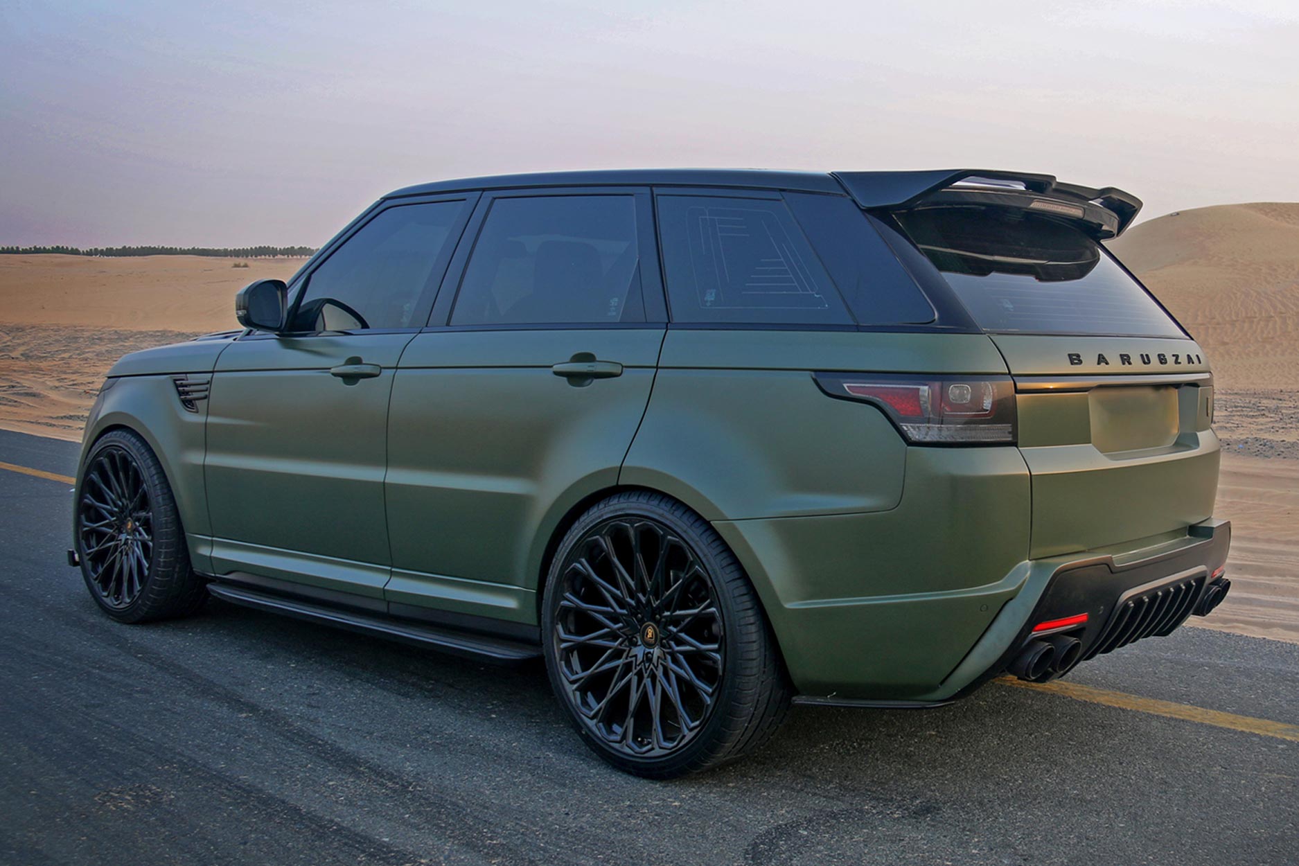 Rear quarter view of a Military Green Range Rover Sport L494 2013-2017. Shot outside a desert. Fitted with Barugzai Majestic 24” alloy wheels, in Gloss Black.