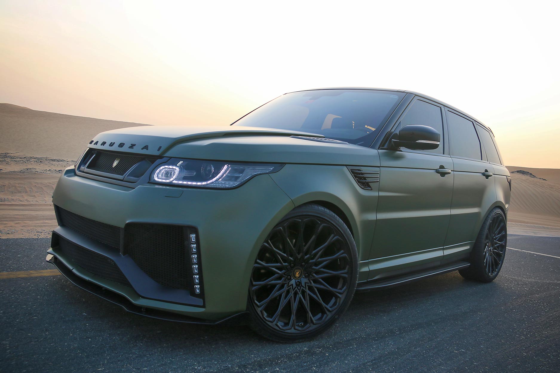 Front quarter view of a Military Green Range Rover Sport L494 2013-2017. Shot outside a desert. Fitted with Barugzai Majestic 24” alloy wheels, in Gloss Black.