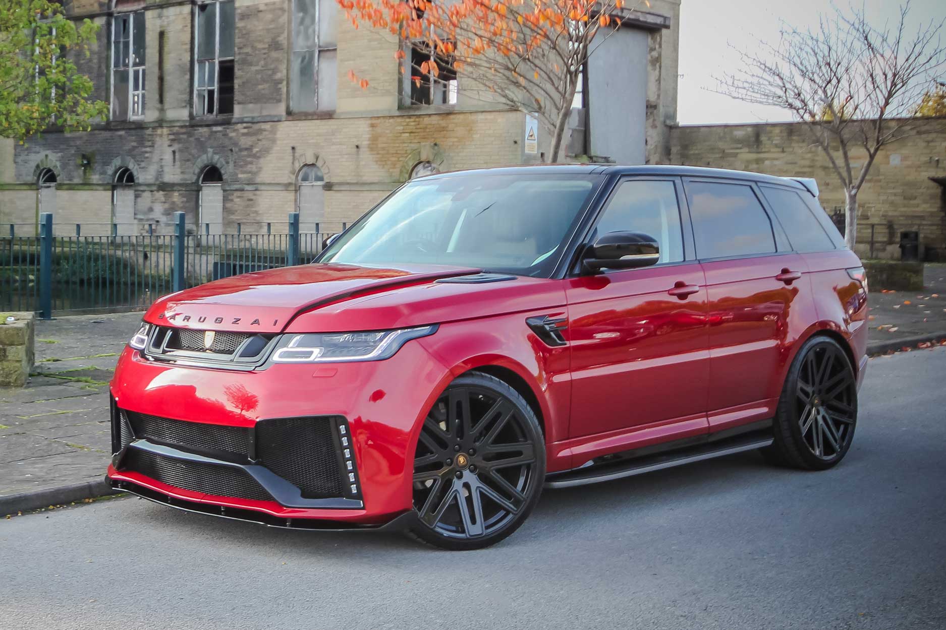 Front quarter view of a Red Range Rover Sport L494 2018-2022. Shot outside an old mill. Fitted with Barugzai EXEL 24” alloy wheels, in Gloss Black.