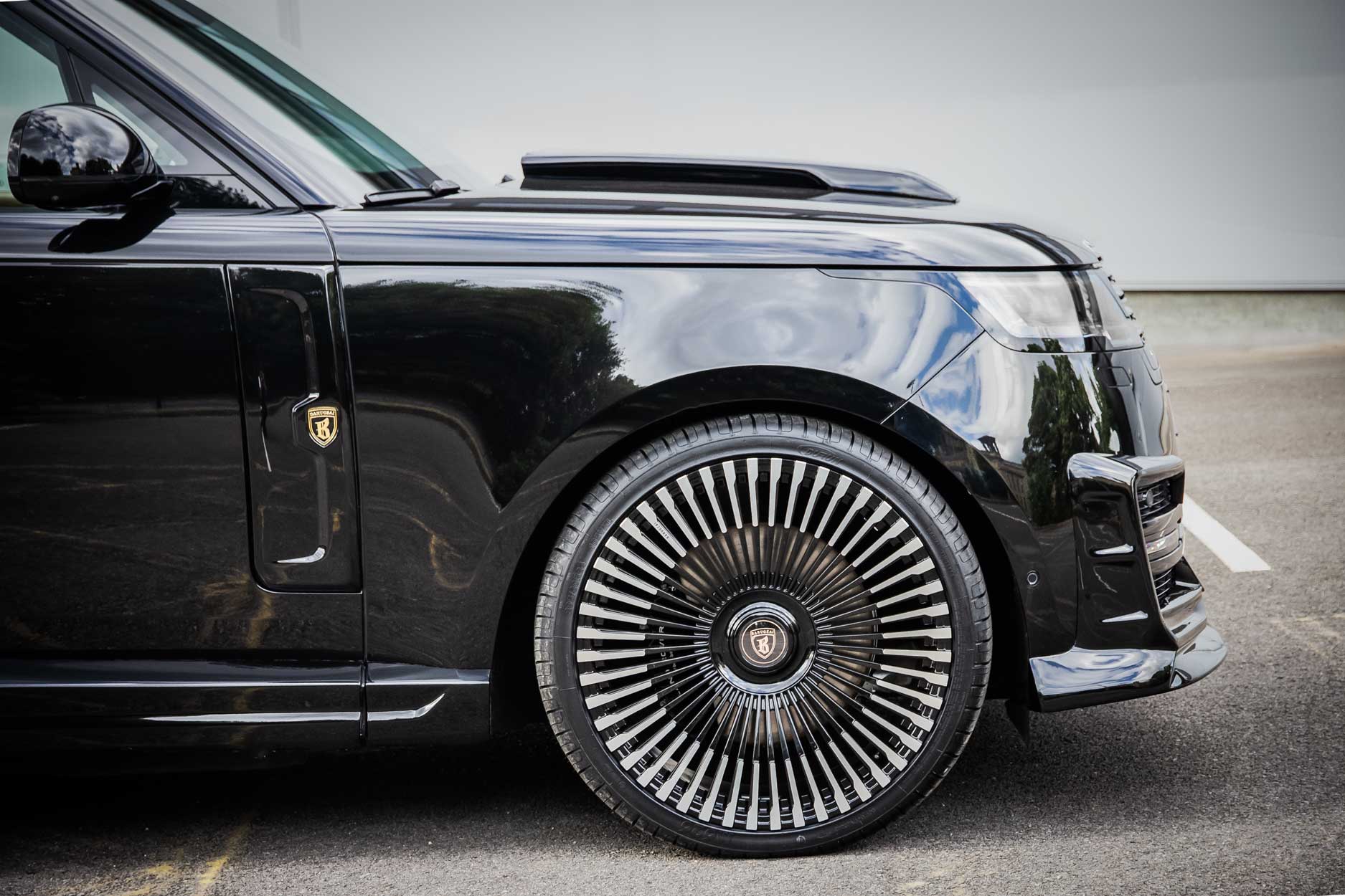 Side view of a Black Range Rover L460 2022+ with a Scoop fitted. Parked on a road with a grey backdrop. Fitted with Barugzai Vortex Forged 24” alloy wheels, in Gloss Black Polished Face.