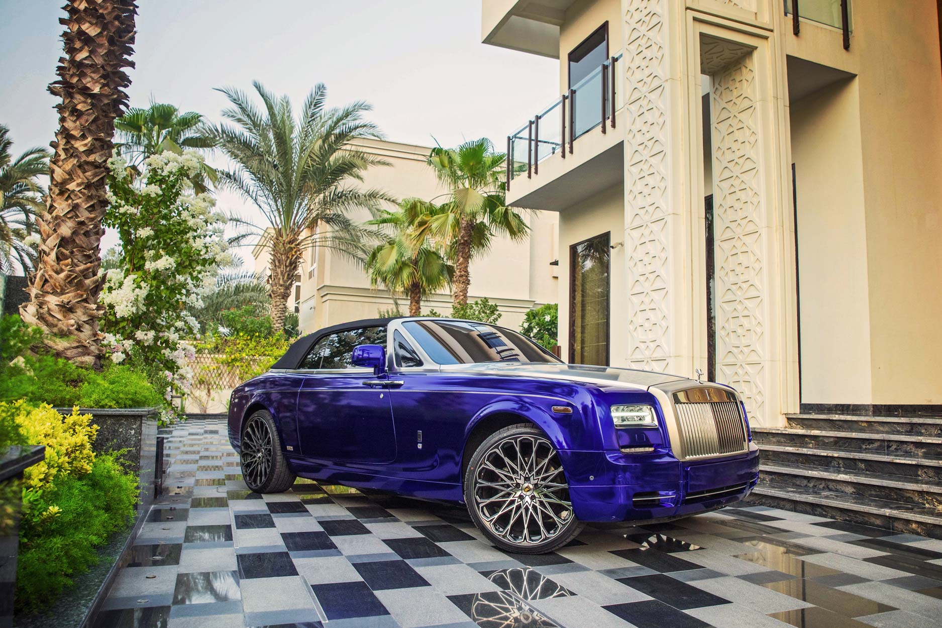 Front quarter view of a Blue Rolls Royce Phantom Drophead 2007-2016. Shot outside a luxurious mansion. Fitted with Barugzai Majestic 24” alloy wheels, in Gloss Black Polished Face.