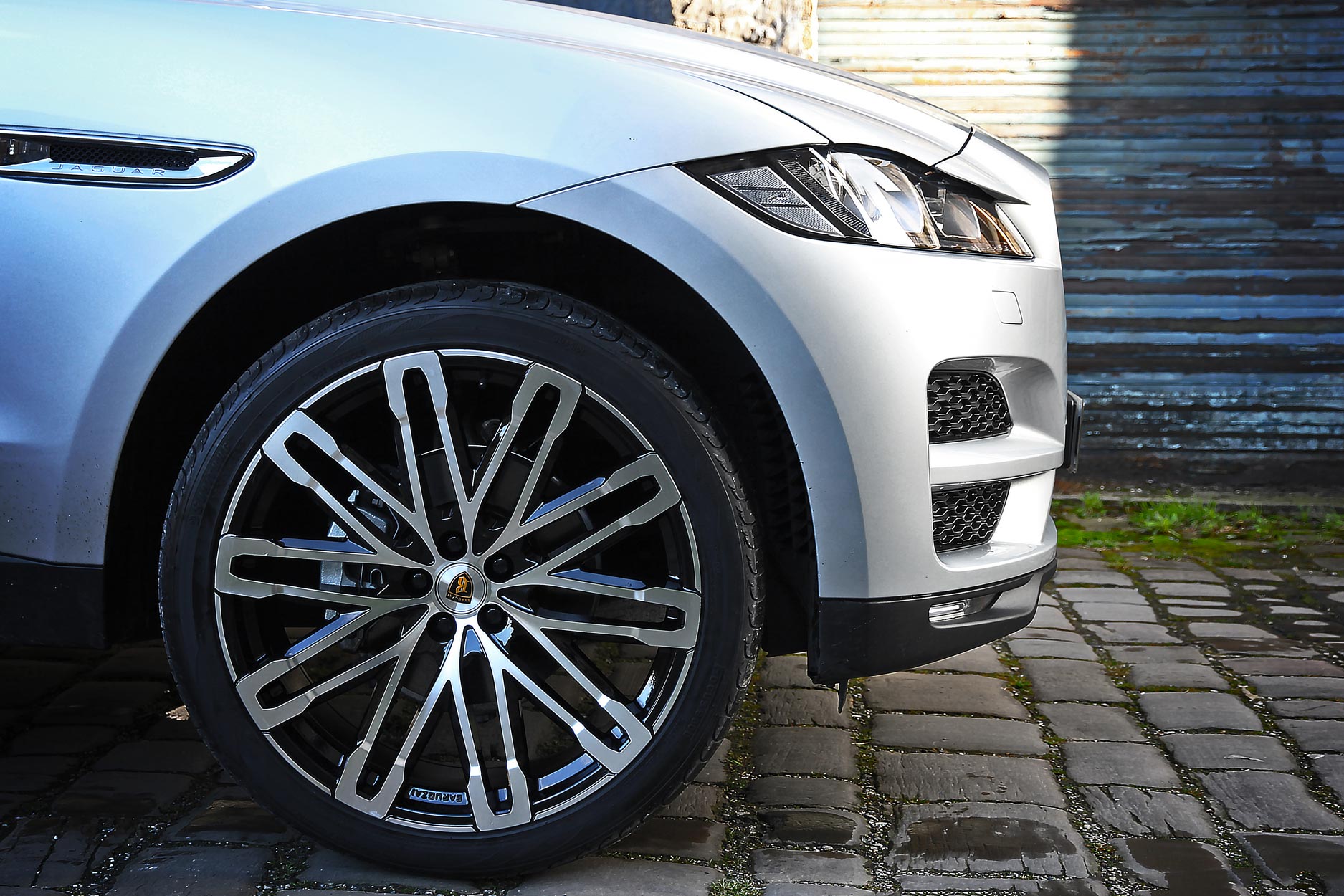 Side detail view of a Silver Jaguar F-Pace 2016+. Shot outside an old mill. Fitted with Barugzai Dawn 22” alloy wheels, in Gloss Black Polished Face.