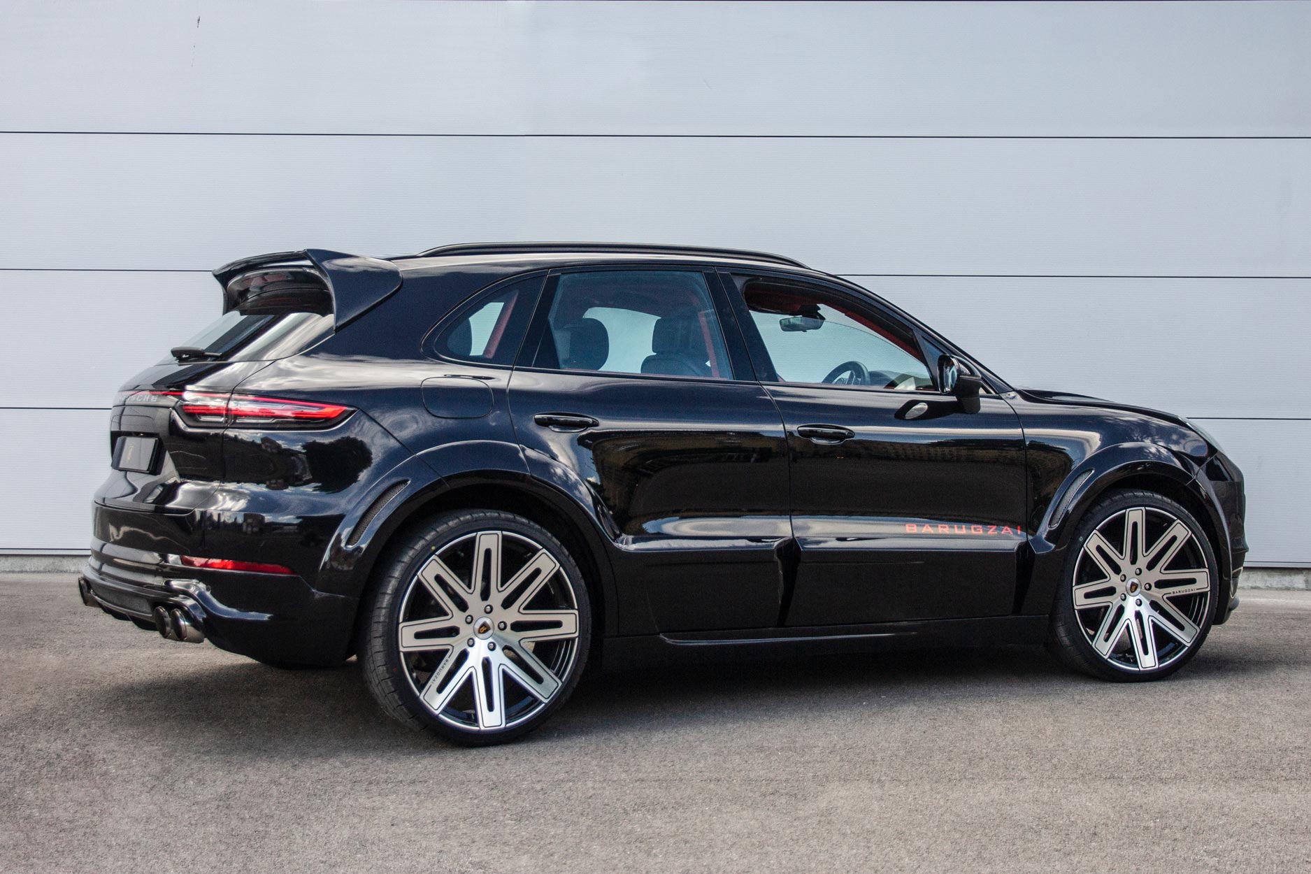 Rear quarter view of a Blue Porsche Cayenne 9YA 2019+. Shot outside a carpark with a grey backdrop. Fitted with Barugzai EXEL 24” alloy wheels, in Gloss Black Polished Face.