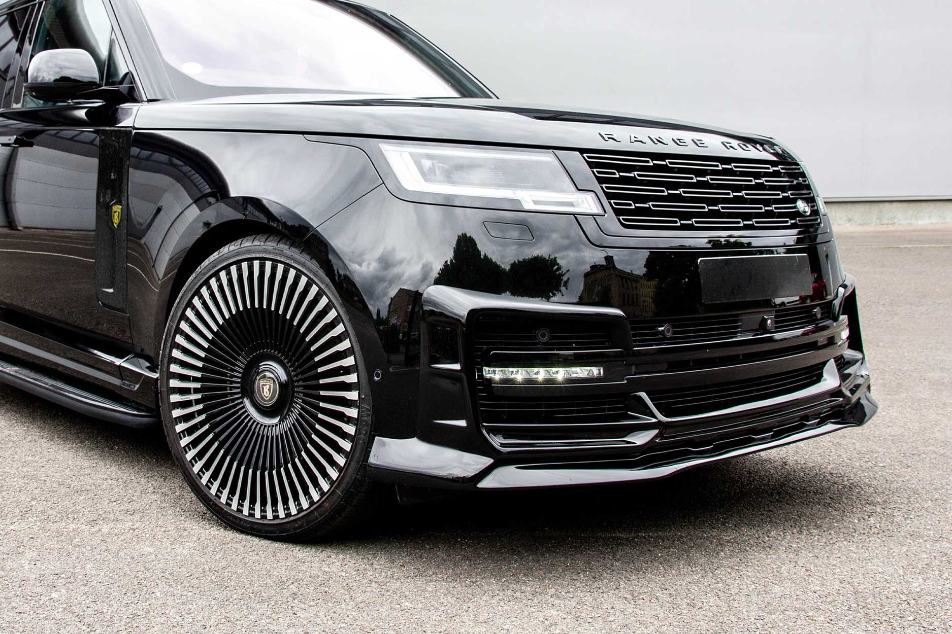 Front quarter detail view of a Black Range Rover L460 2022+. Parked on a road with a grey backdrop. Fitted with Barugzai Vortex Forged 24” alloy wheels, in Gloss Black Polished Face.