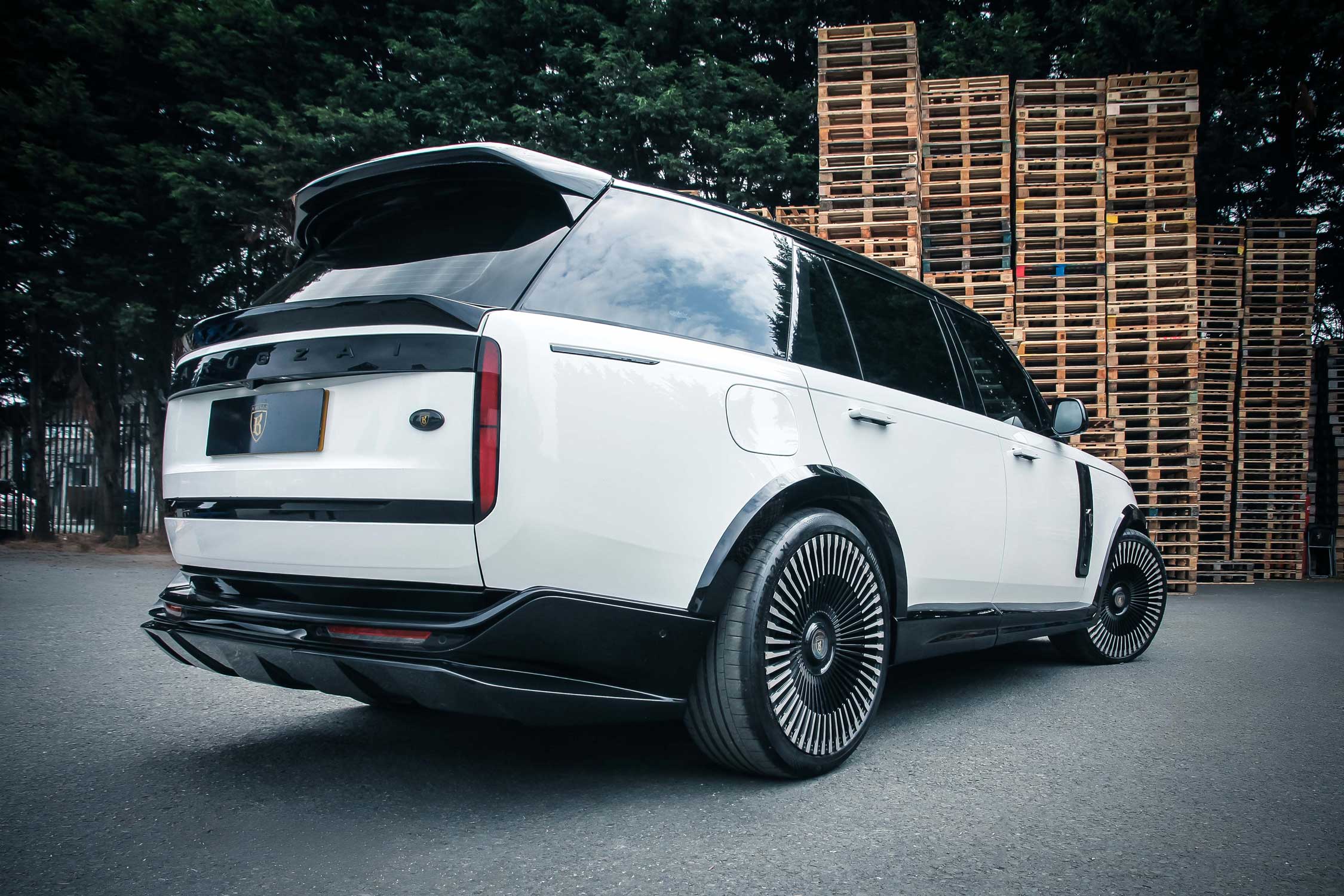 Rear quarter view of a White Range Rover L460 2022+. Shot outside a pallet yard. Fitted with Barugzai Vortex Forged 24” alloy wheels, in Gloss Black Polished Face.