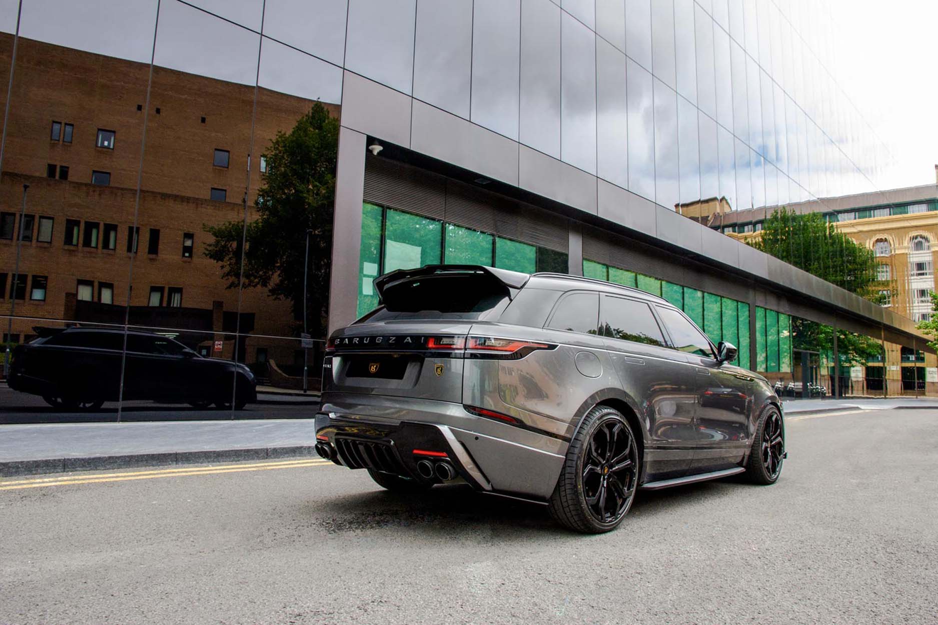 Rear quarter view of a Barugzai Range Rover Velar 2017+ . Shot outside a city high street. Fitted with Barugzai Opium 22” alloy wheels, in Gloss Black