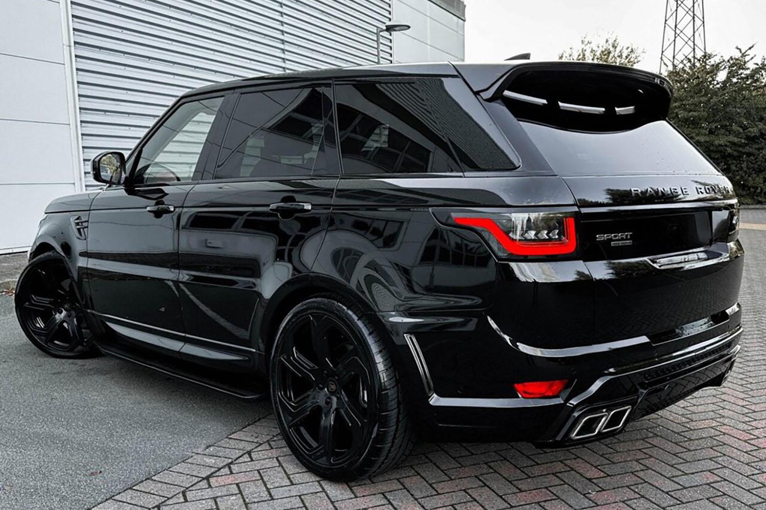 Rear quarter view of a Black Range Rover Sport L494 2018-2022. Shot outside a showroom. Fitted with Barugzai Sabre 22” alloy wheels, in Gloss Black.