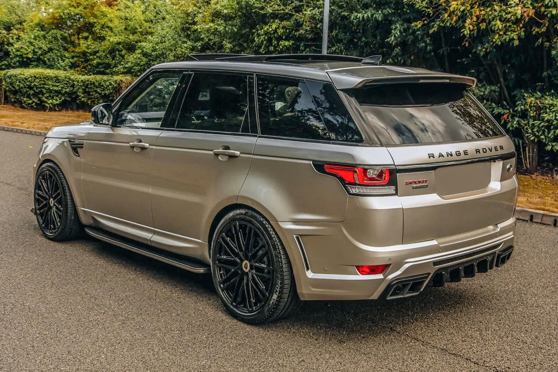 Rear quarter view of a Champagne Range Rover Sport L494 2013-2017. Shot outside with a scenic setting. Fitted with Barugzai Dawn 22” alloy wheels, in Gloss Black.