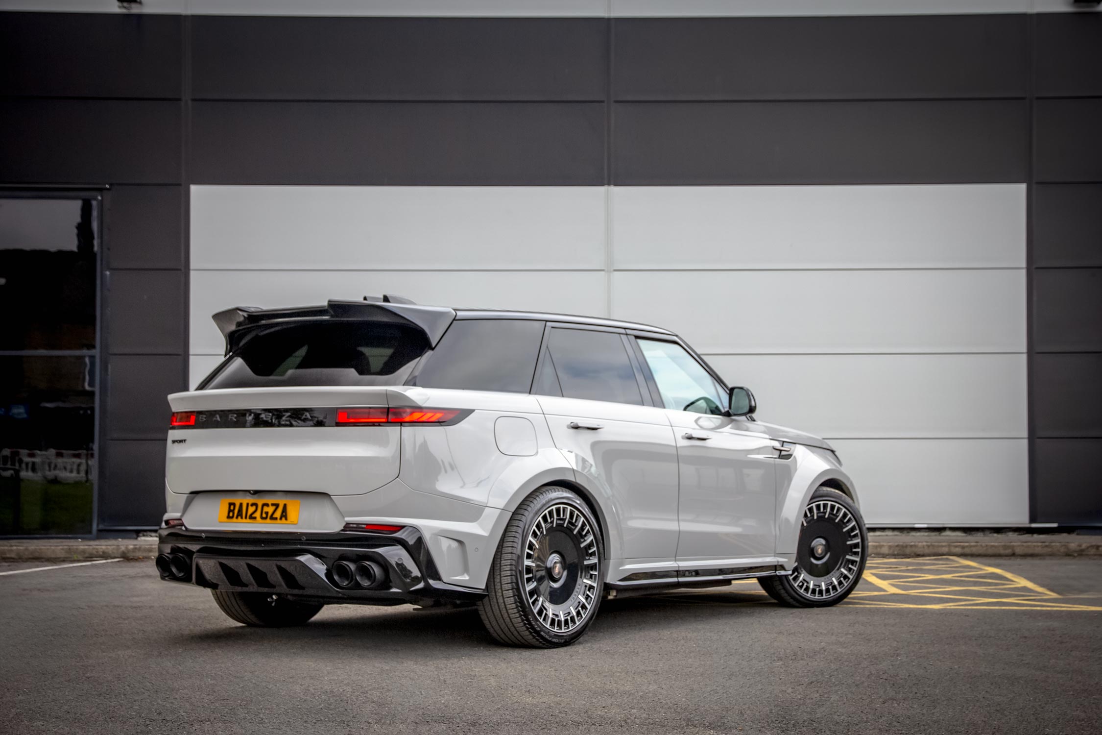 Rear quarter view of a Grey Range Rover Sport L461 2023+. Shot outside a commercial backdrop. Fitted with Barugzai Monoblok 23” alloy wheels, in Gloss Black Polished Face.