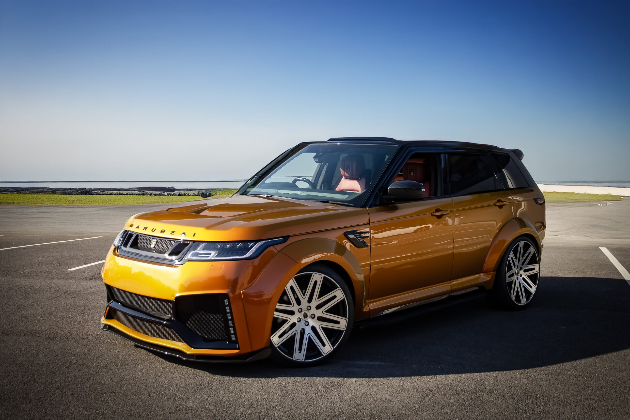 Front quarter view of an Orange Range Rover Sport L494 2018-2022. Shot outside a scenic backdrop. Fitted with Barugzai EXEL 24” alloy wheels, in Gloss Black Polished Face.